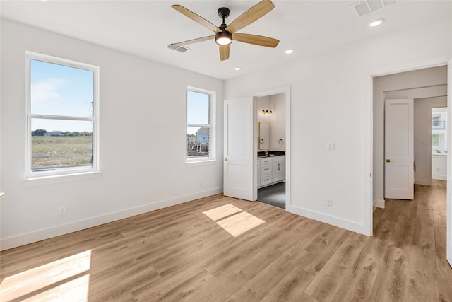 unfurnished bedroom featuring ensuite bathroom, multiple windows, light wood-type flooring, and ceiling fan