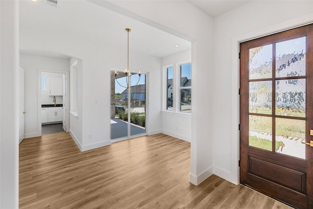 foyer entrance featuring light hardwood / wood-style floors, a notable chandelier, sink, and plenty of natural light