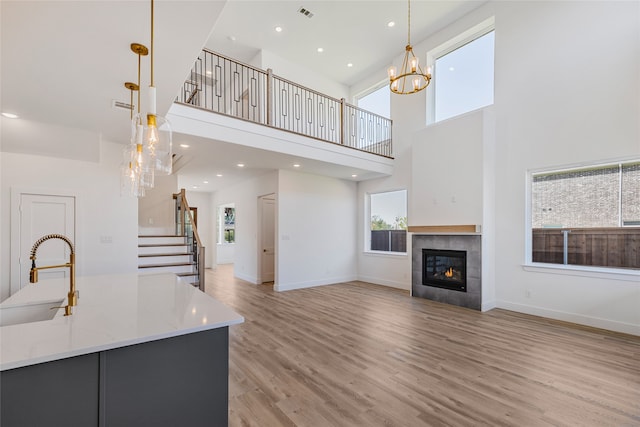 unfurnished living room with sink, a high ceiling, a tiled fireplace, and light hardwood / wood-style floors