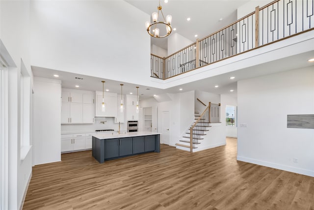 kitchen with a kitchen island with sink, hardwood / wood-style flooring, decorative light fixtures, white cabinetry, and a towering ceiling