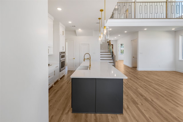 kitchen with a spacious island, white cabinetry, light wood-type flooring, and hanging light fixtures