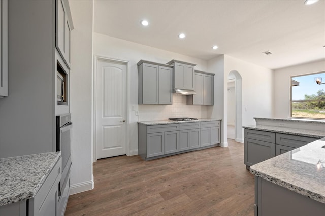 kitchen featuring backsplash, light stone countertops, dark hardwood / wood-style floors, gray cabinets, and stainless steel appliances