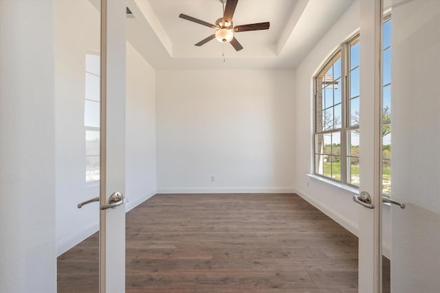 empty room featuring french doors, dark wood-type flooring, a tray ceiling, and ceiling fan