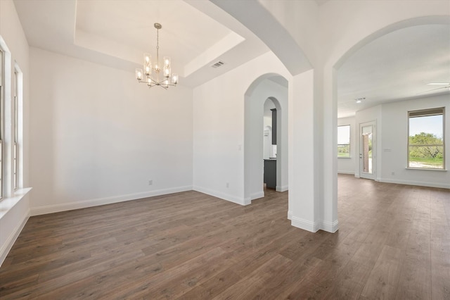 empty room featuring ceiling fan with notable chandelier, dark hardwood / wood-style floors, and a tray ceiling