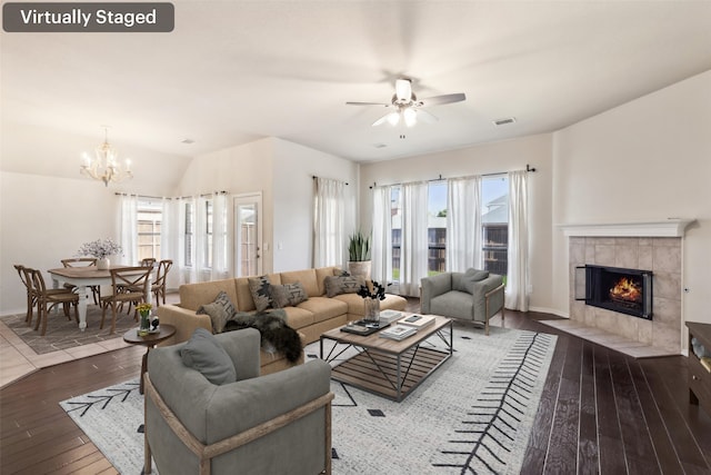 living room featuring dark wood-type flooring, a wealth of natural light, a tile fireplace, and ceiling fan with notable chandelier