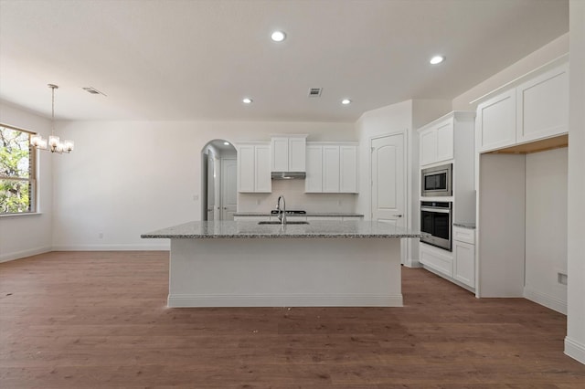 kitchen featuring stainless steel appliances, light stone countertops, wood-type flooring, and a kitchen island with sink