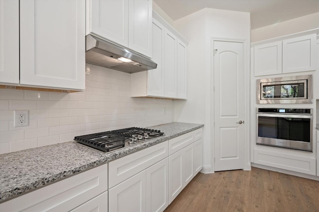 kitchen featuring exhaust hood, light hardwood / wood-style flooring, stainless steel appliances, light stone countertops, and white cabinetry