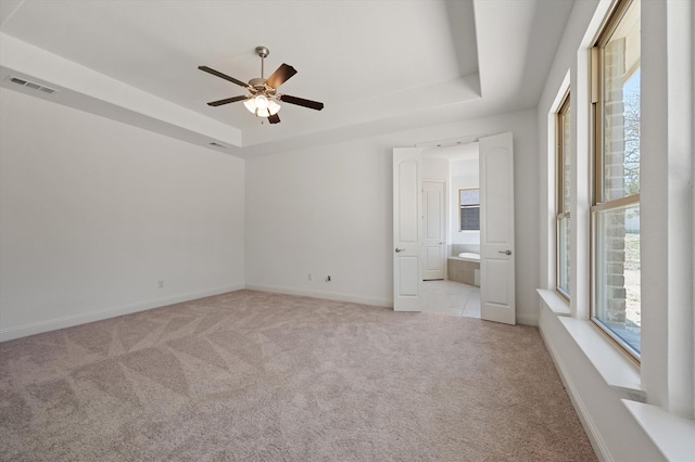 unfurnished bedroom with connected bathroom, ceiling fan, a raised ceiling, and light colored carpet