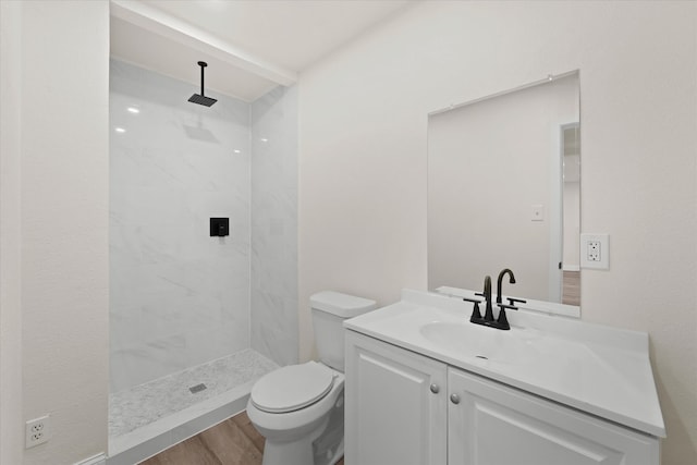 bathroom with toilet, hardwood / wood-style flooring, vanity, and a tile shower