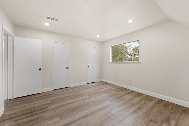 unfurnished bedroom featuring light hardwood / wood-style flooring, multiple closets, and lofted ceiling