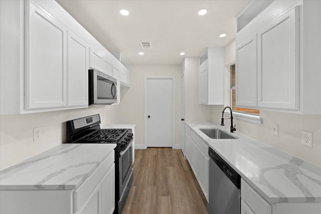 kitchen featuring light stone countertops, appliances with stainless steel finishes, sink, light hardwood / wood-style floors, and white cabinets