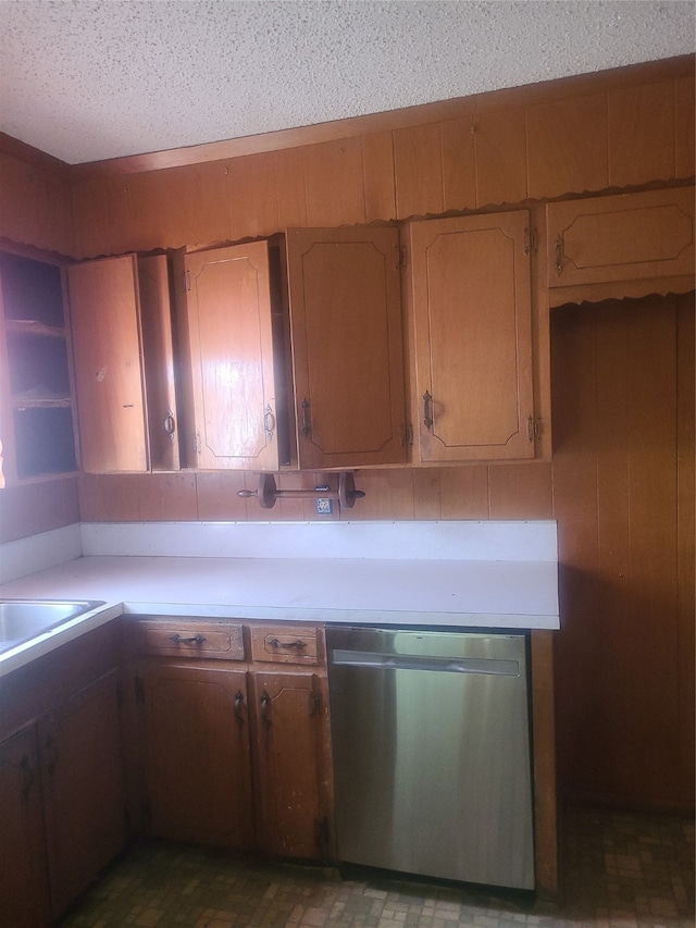 kitchen featuring wood walls, a textured ceiling, and stainless steel dishwasher