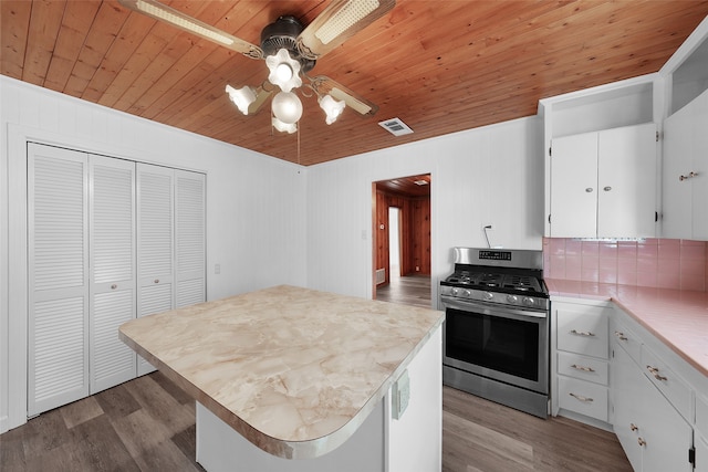 kitchen with hardwood / wood-style floors, white cabinets, wooden walls, stainless steel gas range, and tasteful backsplash