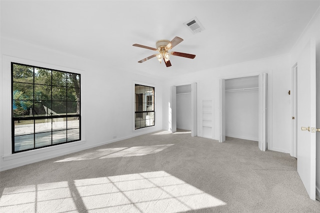 unfurnished bedroom with ceiling fan, light colored carpet, crown molding, and two closets