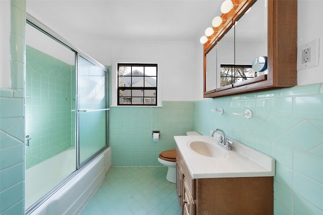 full bathroom featuring tile patterned flooring, bath / shower combo with glass door, toilet, vanity, and tile walls