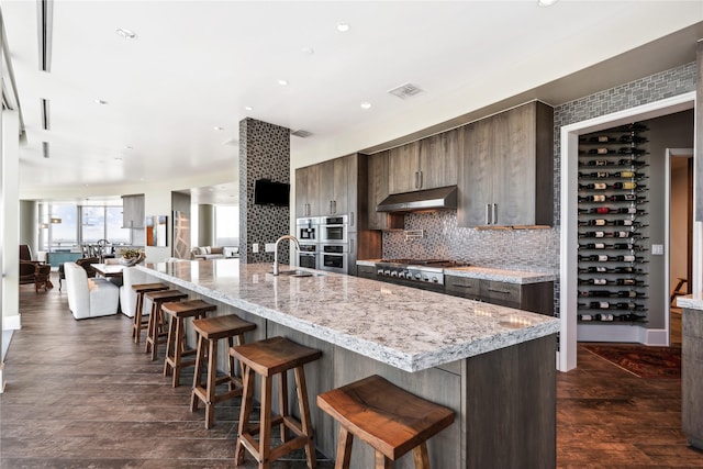 kitchen featuring a breakfast bar, tasteful backsplash, an island with sink, stainless steel appliances, and light stone countertops