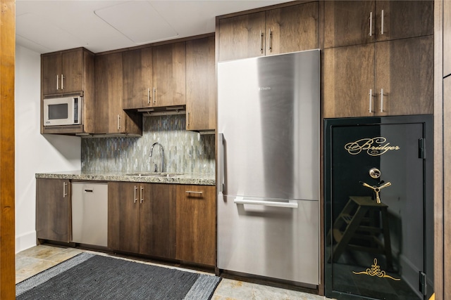 kitchen featuring sink, appliances with stainless steel finishes, backsplash, dark brown cabinets, and light stone counters