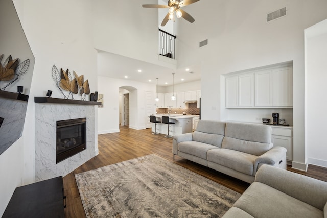 living room with a towering ceiling, hardwood / wood-style floors, ceiling fan, and a high end fireplace