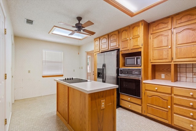 kitchen with ceiling fan, a textured ceiling, black appliances, and a center island