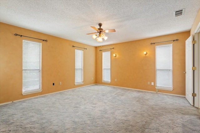 spare room with a textured ceiling, light colored carpet, and ceiling fan