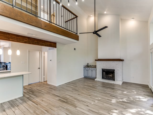 unfurnished living room featuring beam ceiling, ceiling fan, a brick fireplace, a towering ceiling, and light hardwood / wood-style floors