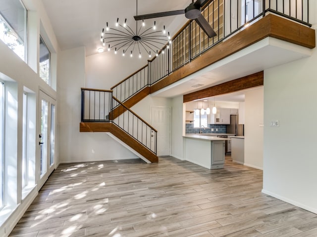 unfurnished living room with a high ceiling, french doors, sink, ceiling fan, and light hardwood / wood-style floors