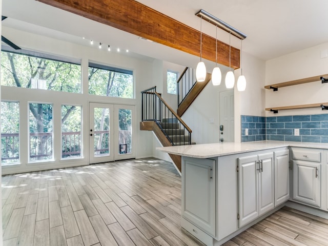 kitchen with white cabinets, tasteful backsplash, decorative light fixtures, light hardwood / wood-style floors, and light stone counters