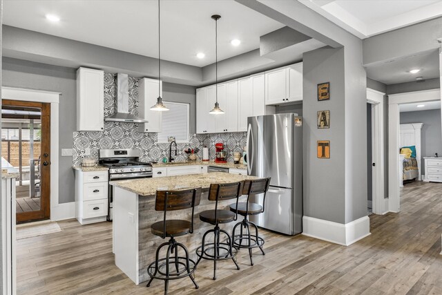 kitchen with wall chimney range hood, a center island, white cabinetry, appliances with stainless steel finishes, and light hardwood / wood-style floors