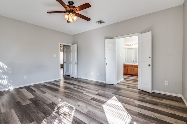 unfurnished bedroom featuring ensuite bath, dark wood-type flooring, and ceiling fan