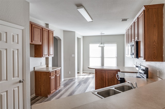 kitchen featuring kitchen peninsula, hanging light fixtures, appliances with stainless steel finishes, light hardwood / wood-style floors, and sink