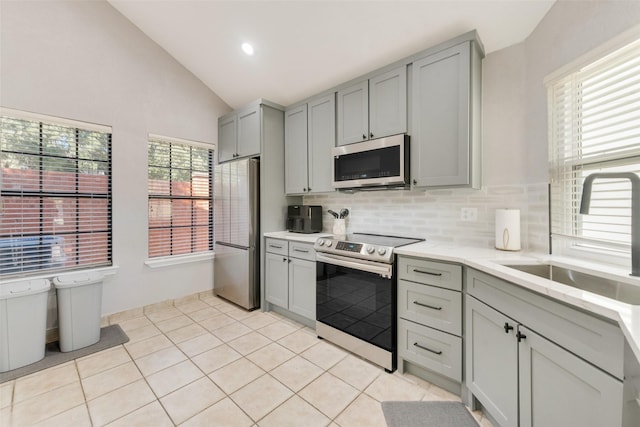 kitchen with decorative backsplash, stainless steel appliances, vaulted ceiling, sink, and gray cabinets