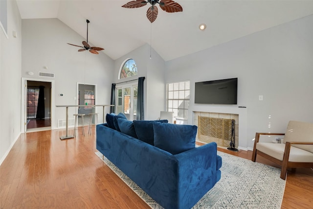 living room featuring a tile fireplace, ceiling fan, high vaulted ceiling, and hardwood / wood-style flooring