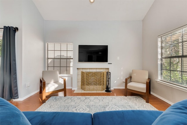 living room with a tile fireplace, lofted ceiling, and hardwood / wood-style flooring