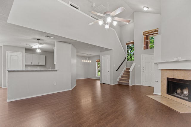 unfurnished living room with dark hardwood / wood-style floors, high vaulted ceiling, a tile fireplace, and ceiling fan