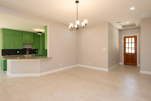 kitchen featuring tasteful backsplash, green cabinetry, decorative light fixtures, kitchen peninsula, and light stone countertops