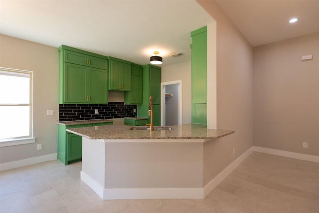 kitchen with light stone countertops, sink, green cabinets, and kitchen peninsula