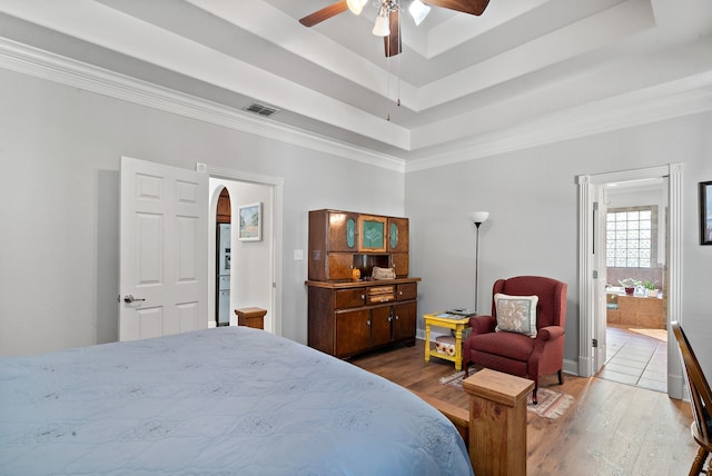 bedroom featuring a tray ceiling, ensuite bath, hardwood / wood-style floors, crown molding, and ceiling fan