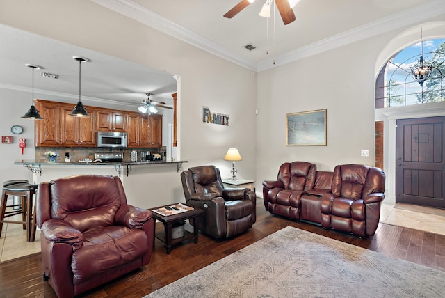 living room featuring dark wood-type flooring, crown molding, and ceiling fan with notable chandelier