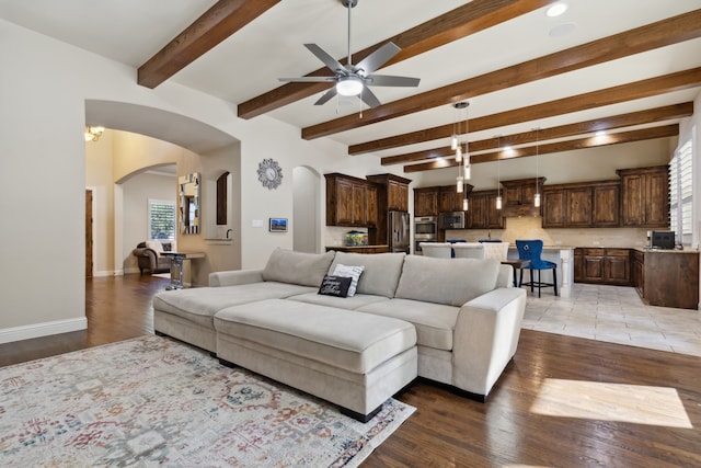 living room with a wealth of natural light, beamed ceiling, ceiling fan with notable chandelier, and light wood-type flooring