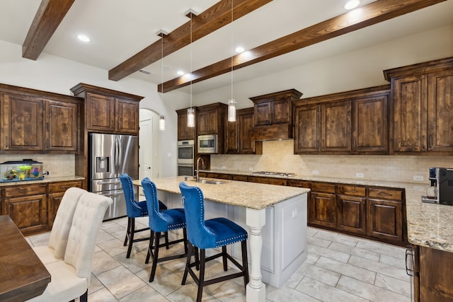 kitchen with sink, stainless steel appliances, light stone counters, beamed ceiling, and a kitchen island with sink