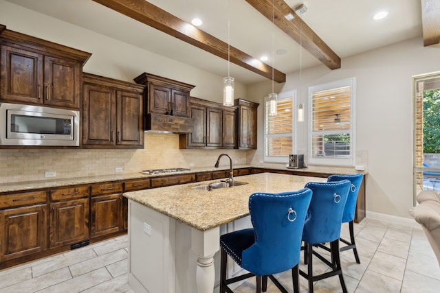 kitchen with sink, beamed ceiling, a kitchen bar, a kitchen island with sink, and appliances with stainless steel finishes