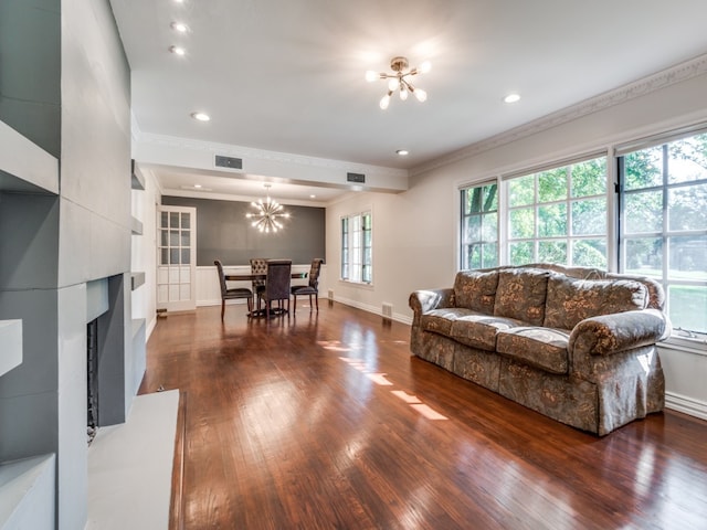 living room with dark wood-type flooring, a fireplace, a notable chandelier, and crown molding