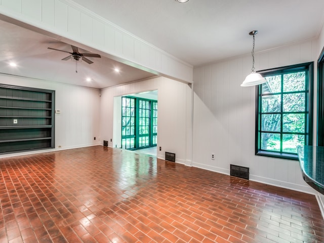 unfurnished living room with ornamental molding, wooden walls, and ceiling fan