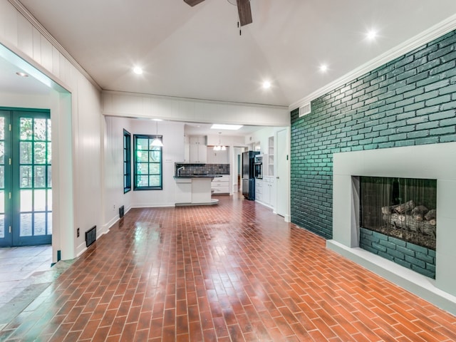 unfurnished living room with ornamental molding, ceiling fan, brick wall, and a brick fireplace