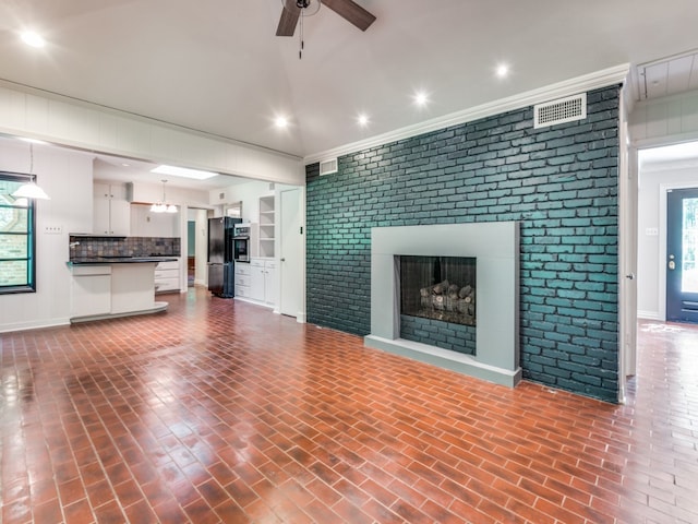 unfurnished living room with ornamental molding, ceiling fan, brick wall, and a brick fireplace