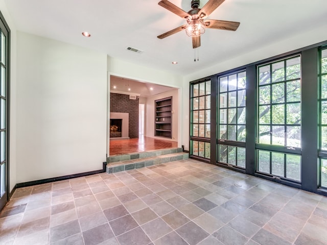 spare room with a fireplace, built in features, and ceiling fan