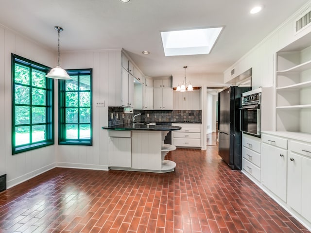 kitchen featuring black appliances, a breakfast bar, a skylight, white cabinets, and tasteful backsplash