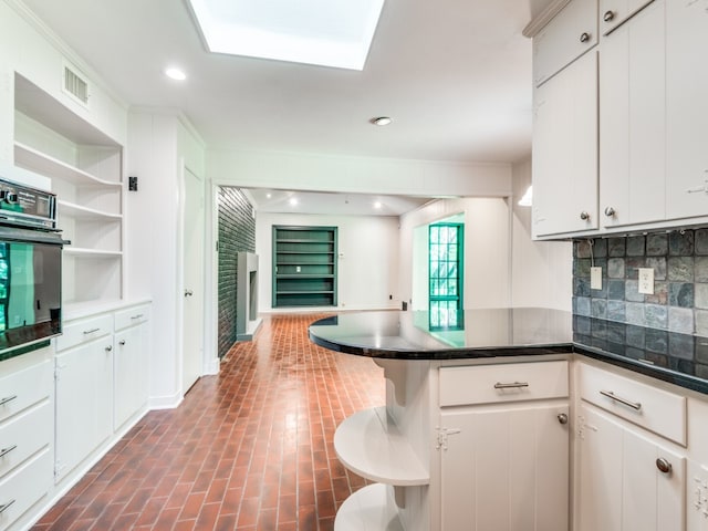 kitchen featuring white cabinetry, backsplash, oven, and kitchen peninsula