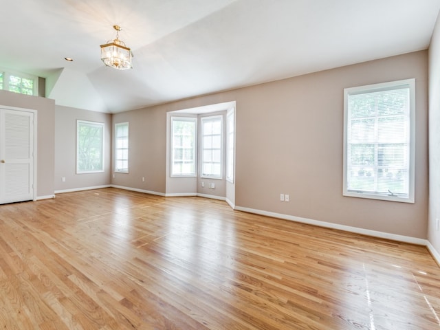 unfurnished room with light hardwood / wood-style floors, a notable chandelier, lofted ceiling, and a wealth of natural light