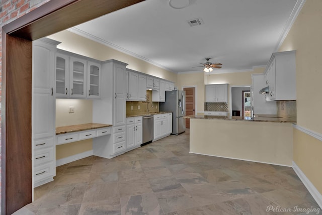 kitchen with white cabinetry, built in desk, appliances with stainless steel finishes, ornamental molding, and ceiling fan